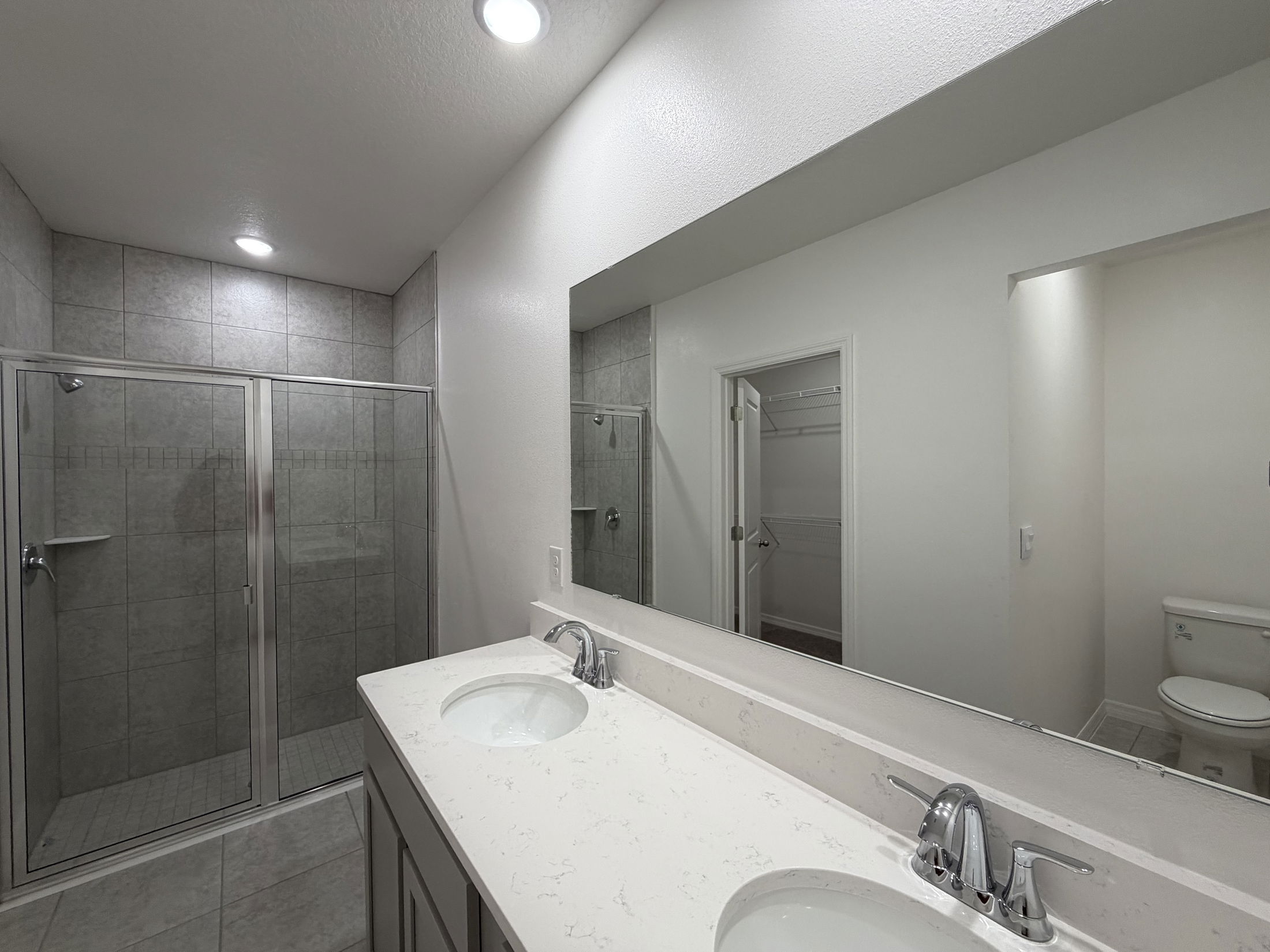Modern bathroom featuring a dual-sink vanity top, spacious glass-enclosed shower, and neutral-toned tile design.
