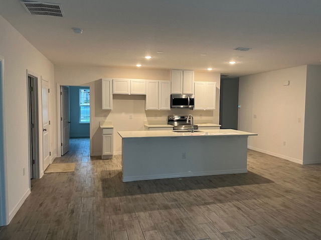 Spacious modern kitchen with white cabinetry, recessed lighting, and a large island, featuring stainless steel appliances and wood-style flooring.