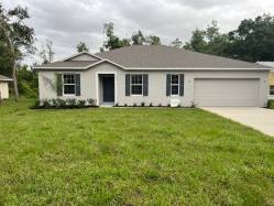 Single-story suburban home with a gray roof, white exterior, attached garage, and surrounding greenery.