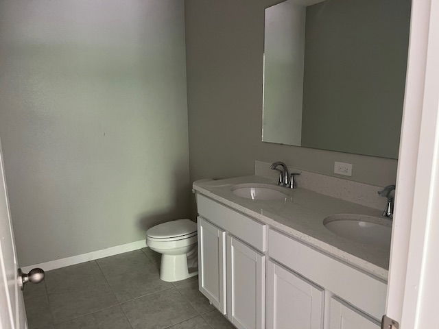 A modern, minimalist bathroom featuring a double sink vanity with white cabinetry, large wall mirror, and adjacent toilet against light gray walls.