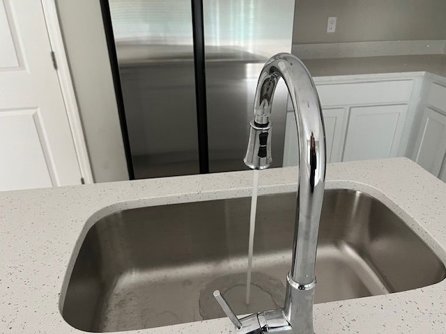 Modern kitchen sink with a chrome faucet and running water, set against a sleek countertop and white cabinetry.