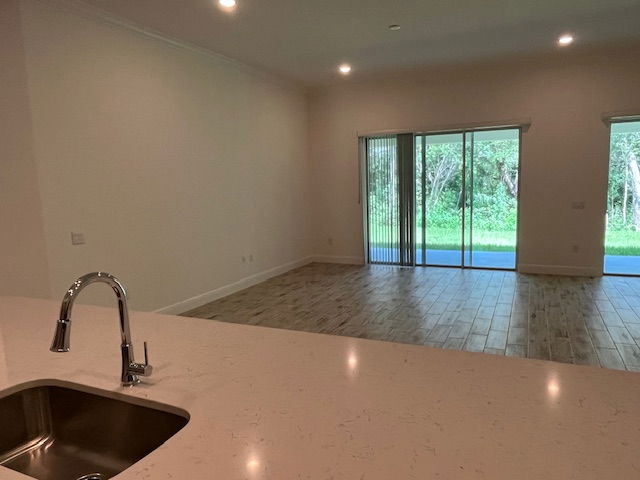 Modern open-plan kitchen and living room interior with a sleek sink, polished countertops, and large sliding glass doors leading to a serene outdoor view.