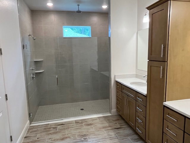 Modern bathroom with spacious glass shower, wooden cabinetry, and tile flooring.