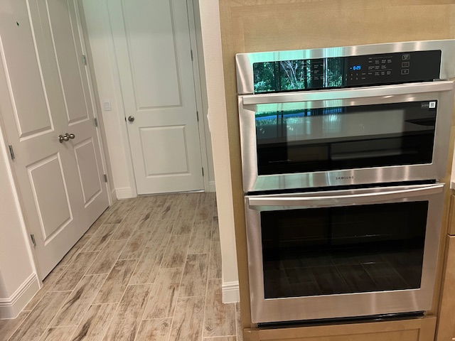 Modern kitchen with Samsung stainless steel double wall oven and wood-look tile flooring.