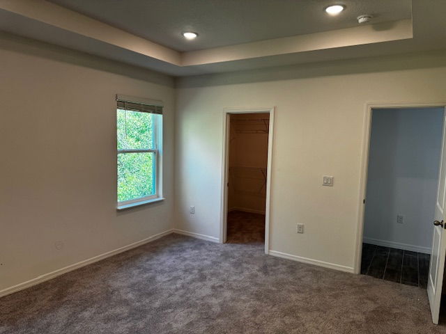 Empty bedroom with carpet flooring, recessed lighting, a window, and two doorways leading to a walk-in closet and adjacent room.