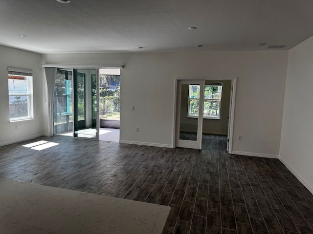 Empty modern living room with wood-look tile flooring, sliding glass doors, and large windows.