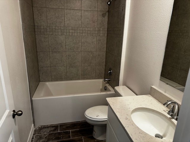 Modern bathroom with a tiled shower-bathtub combo, sleek sink, and dark wood floor tiles.