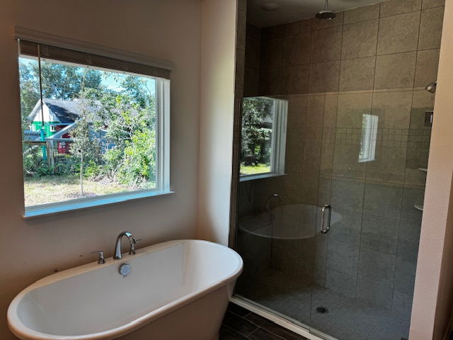 Modern bathroom with a white freestanding bathtub and a glass-enclosed walk-in shower beside a window with a garden view.