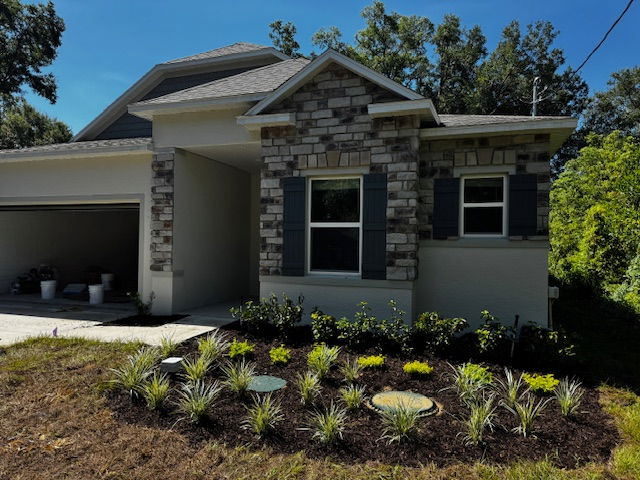 Modern single-story house with stone accents and a landscaped front yard under a clear blue sky.