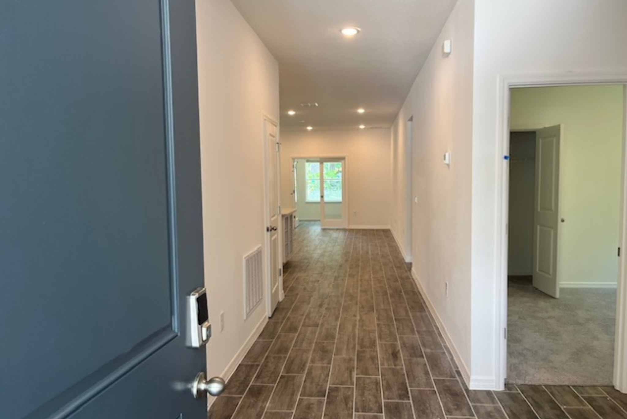 Modern home entrance hallway with wooden flooring and bright natural light from large glass doors.