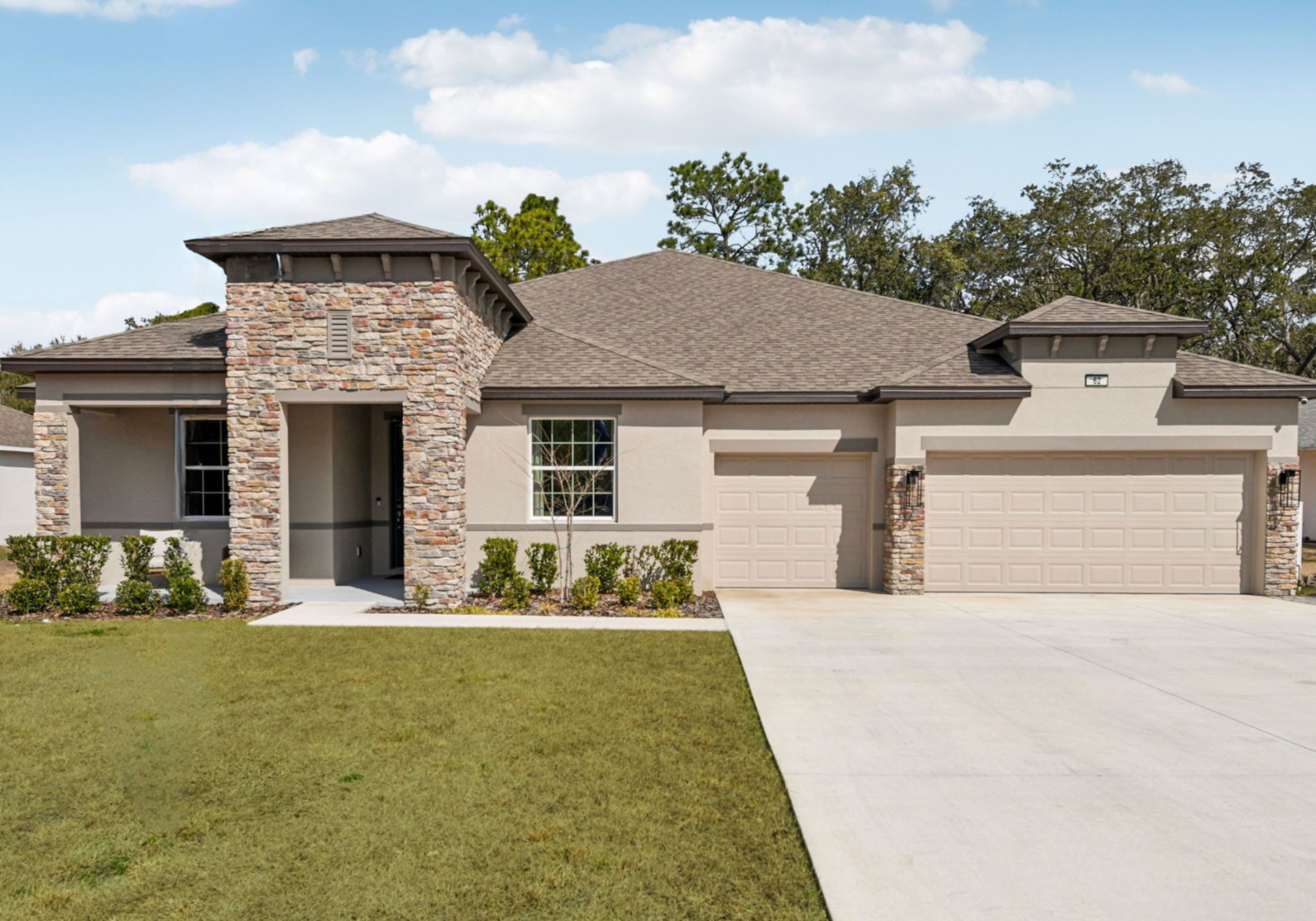 A single-story house with a stone-accented entrance and a spacious driveway surrounded by green landscaping.