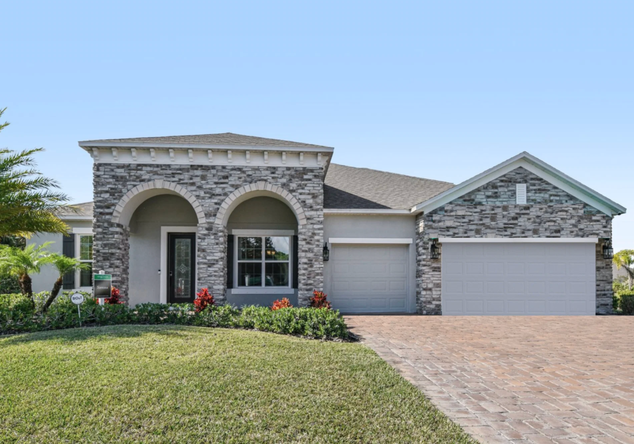 A modern single-story home with a stone exterior, arched entryway, and a well-maintained lawn.
