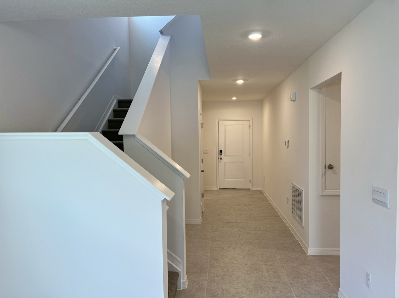 Modern, minimalist white hallway with stairs and closed doors, featuring recessed lighting and tiled floor.
