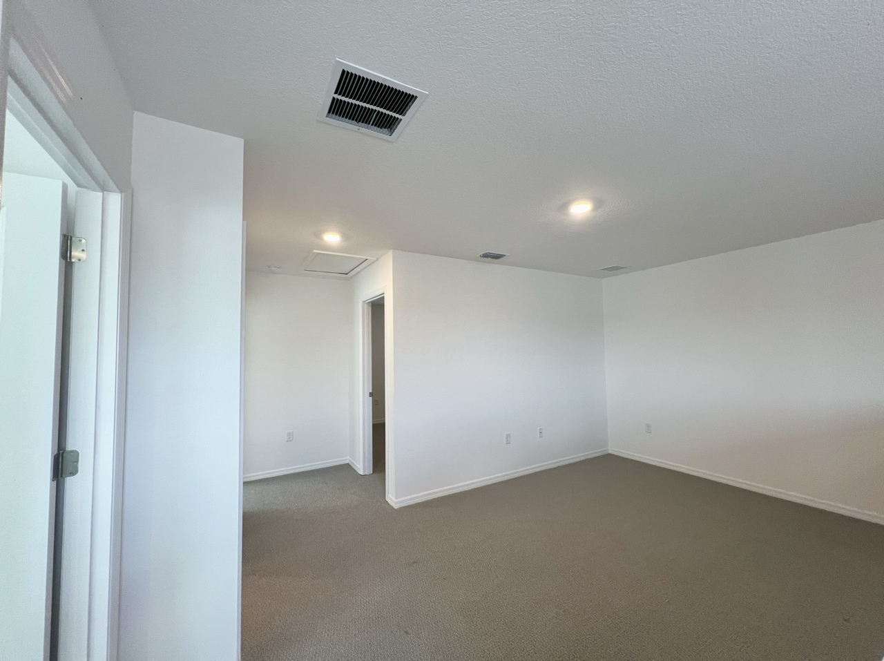 Empty, white-walled room with beige carpet, recessed lighting, and a visible doorway.