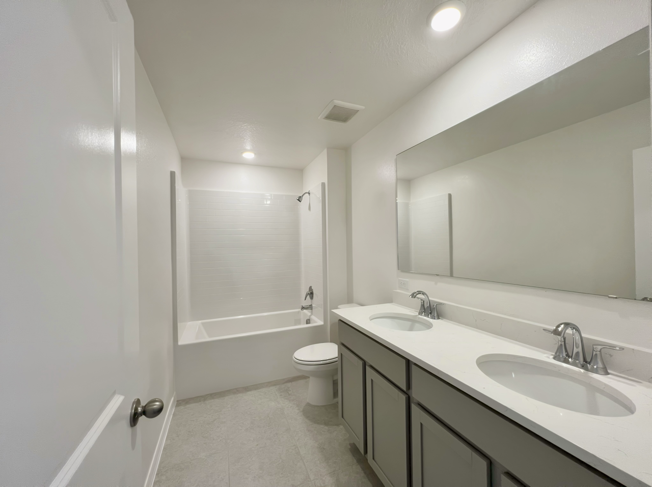 Modern bathroom with dual sinks, a large mirror, tiled shower and bathtub, and neutral-toned cabinetry.