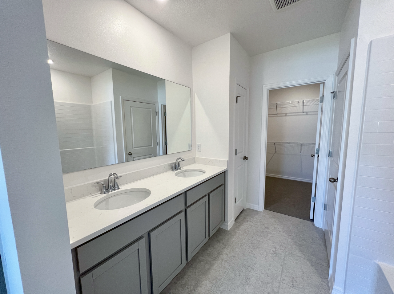 Modern bathroom with a dual-sink vanity, large mirror, and adjacent walk-in closet.