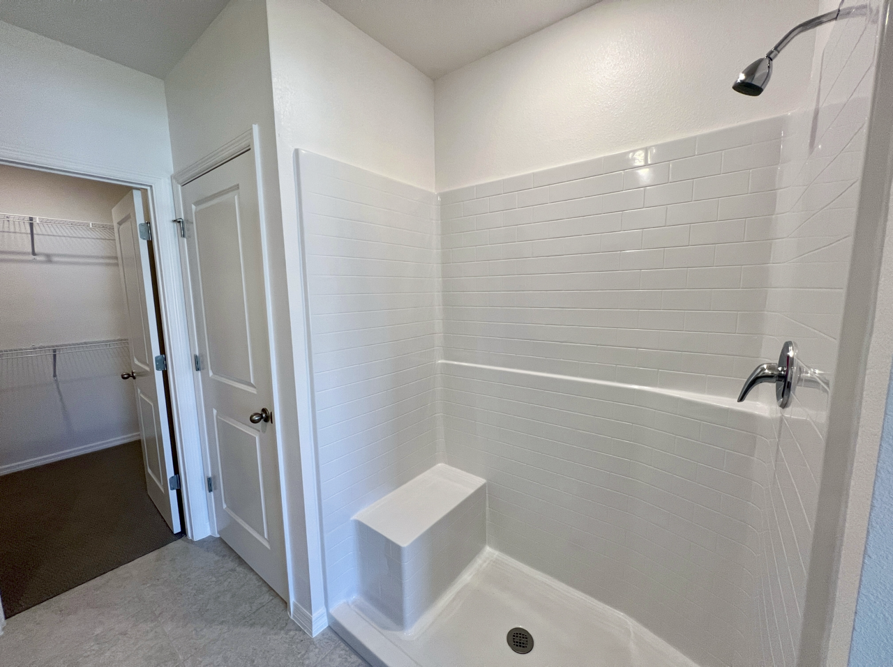 Modern white tiled shower with built-in bench and chrome fixtures next to a closet door.