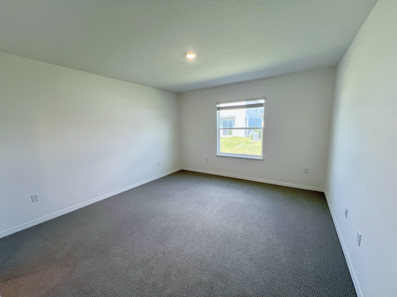 Bright, empty carpeted room with a single window and white walls, ideal for customization.