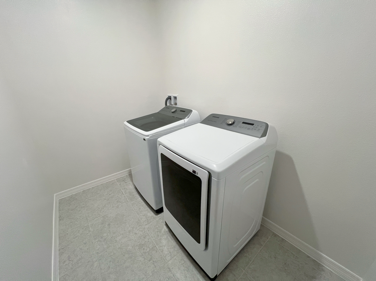 Modern laundry room with white top-load washer and front-load dryer on a tile floor.