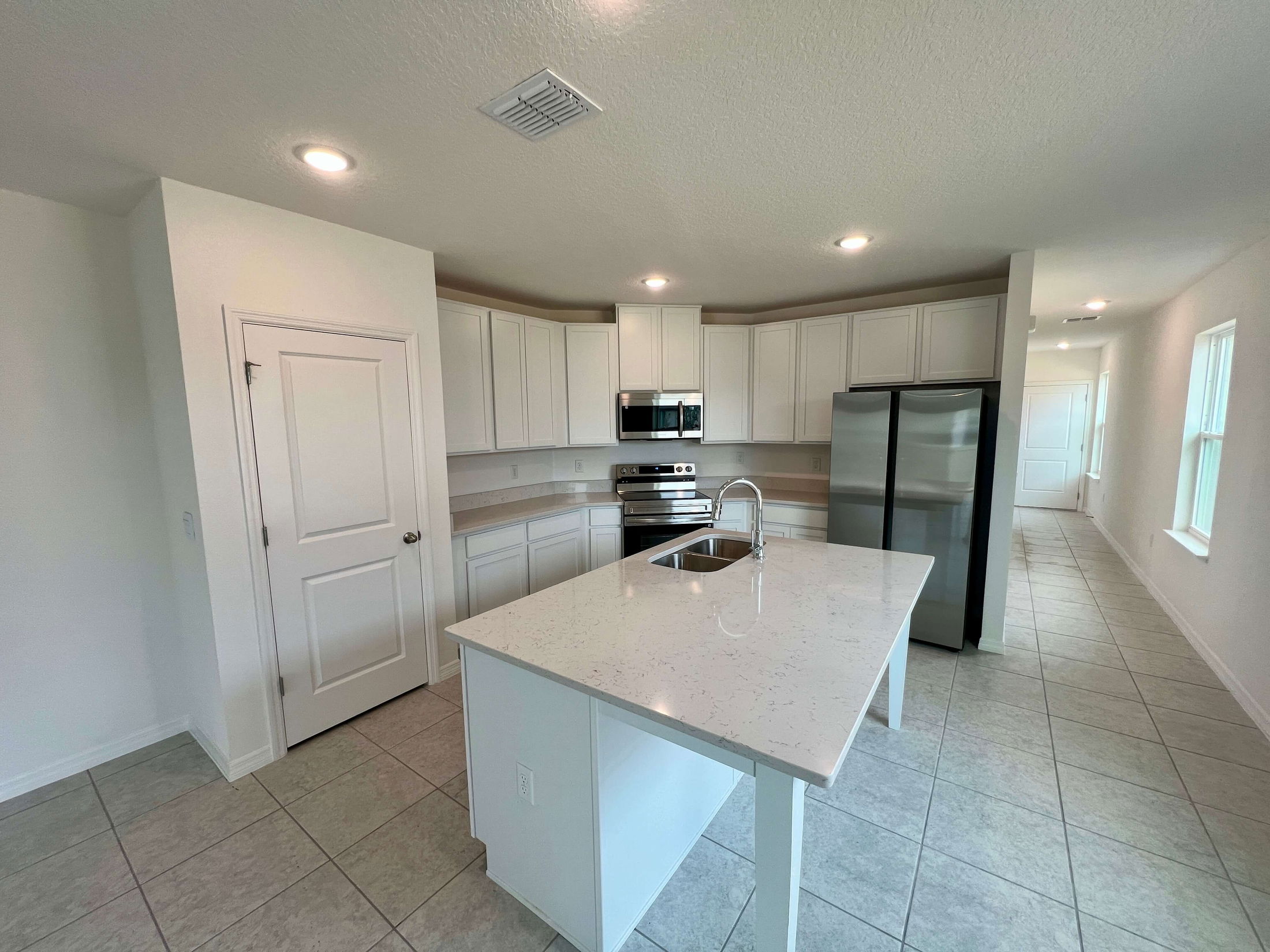 Modern kitchen with white cabinets, stainless steel appliances, and a large island featuring a built-in sink in a spacious open floor plan.