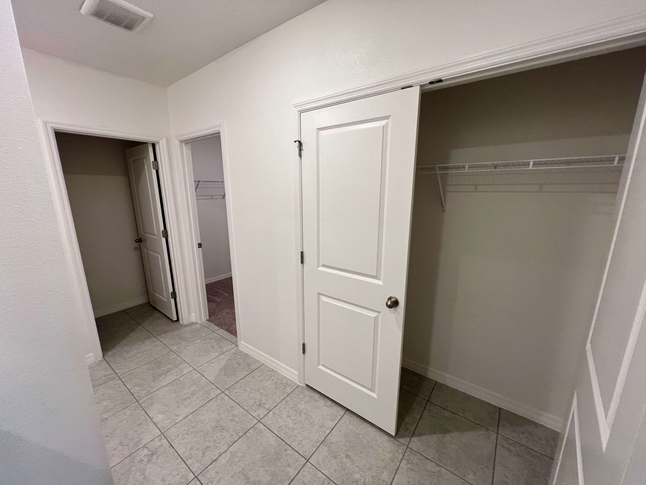 Empty hallway with tiled flooring and open closets in a modern home.