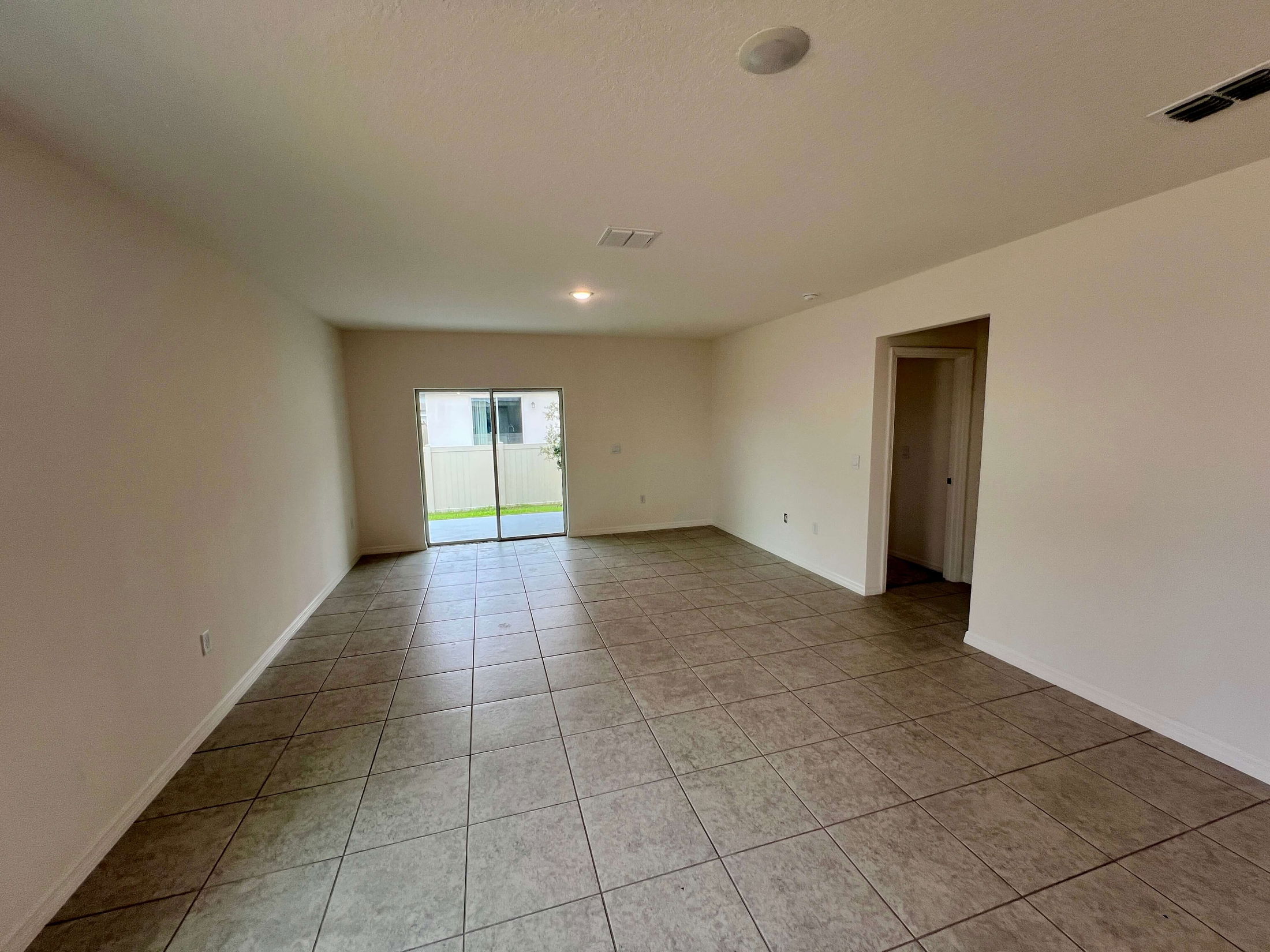 Empty room with beige tiled flooring and a sliding glass door leading to an outdoor area.