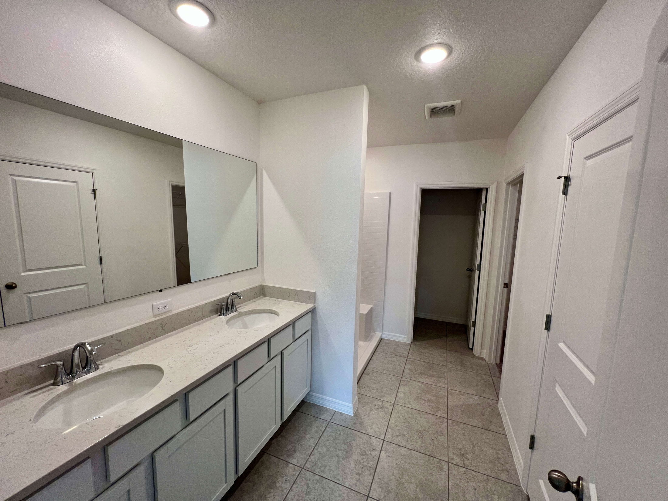 Modern bathroom with dual sinks, large mirror, and tiled flooring.