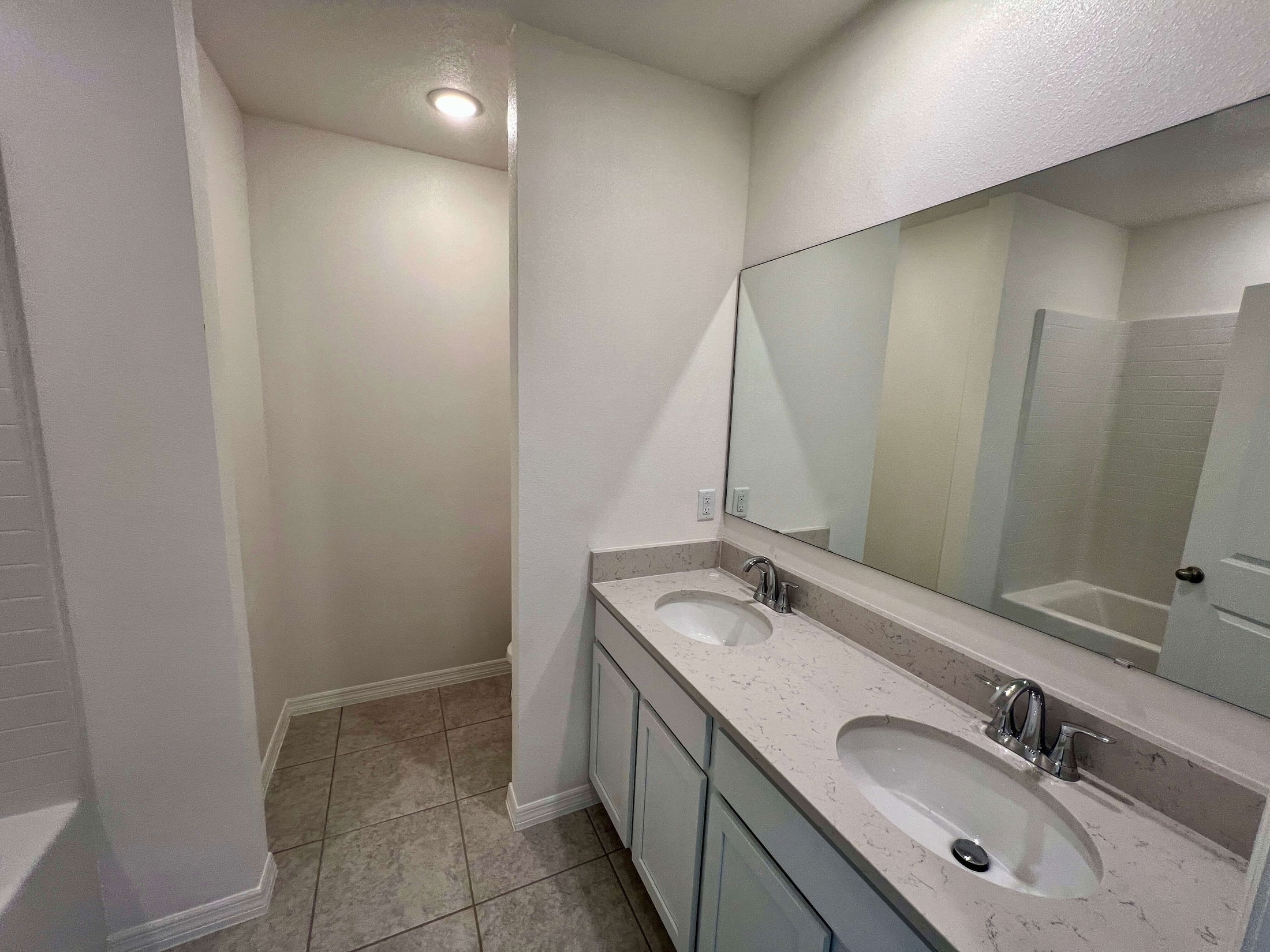 Modern bathroom with large mirror, double sinks, and neutral tile flooring.