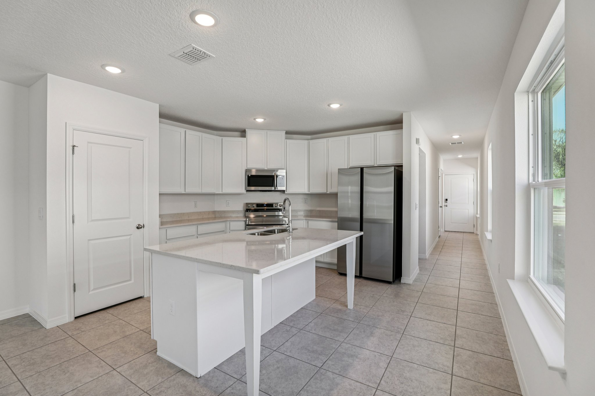 Modern kitchen with sleek white cabinetry, a large island, stainless steel appliances, and tiled flooring illuminated by recessed lighting.