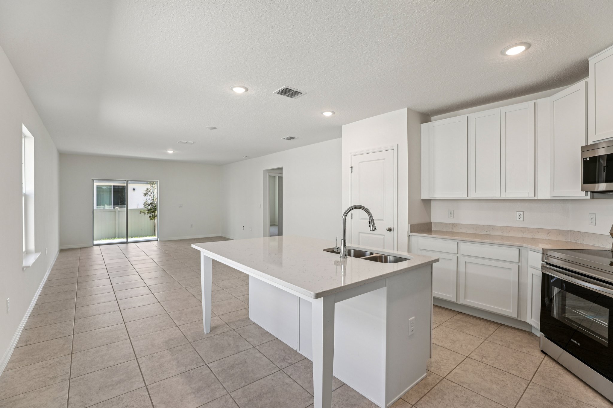 Modern open-concept kitchen and living area with white cabinetry, a central island, and large tile flooring.