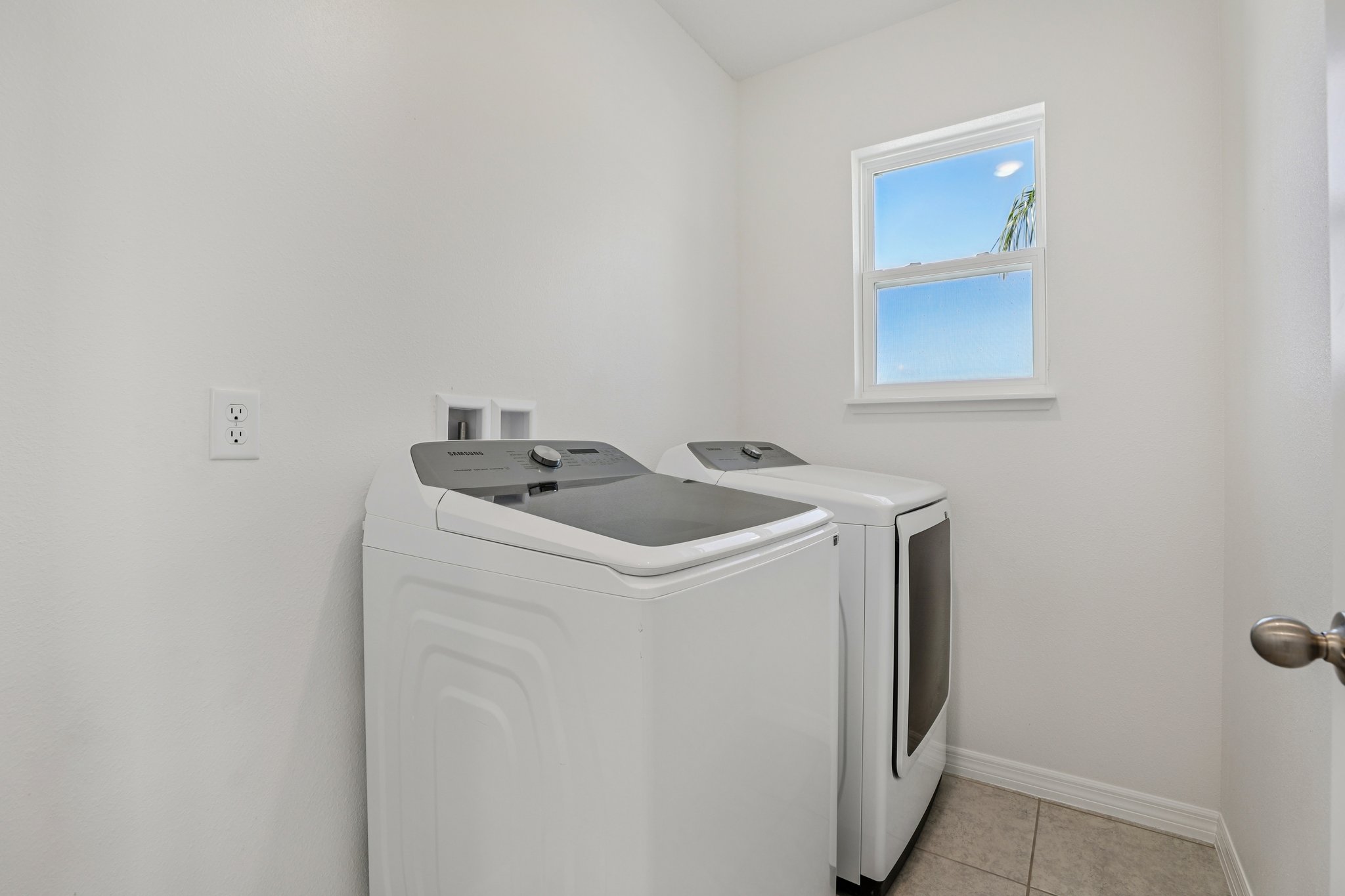 Modern laundry room with a top-load washer and front-load dryer beneath a window, set against a clean white wall.