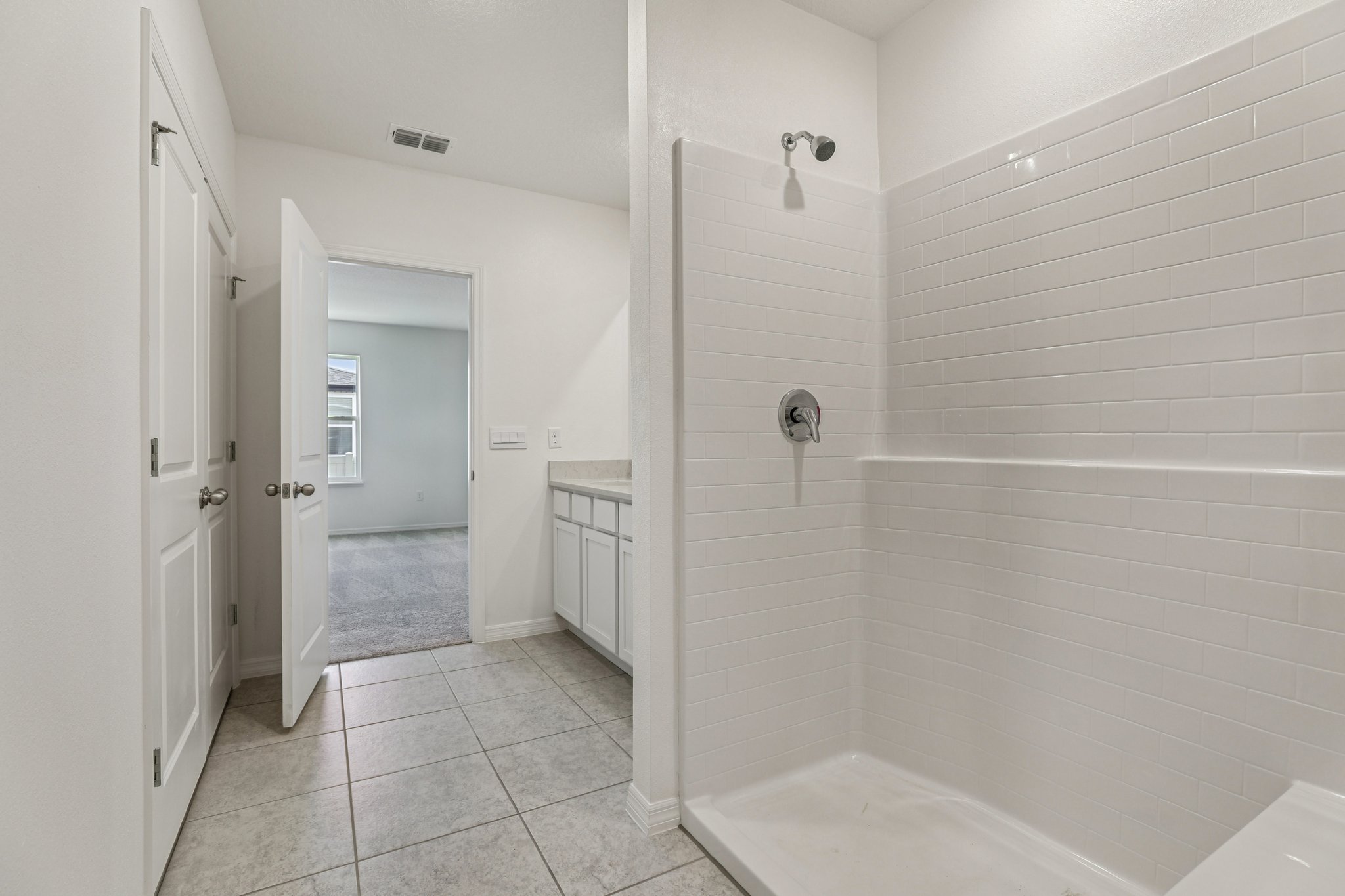 Modern bathroom with tiled shower, white cabinets, and a view into a carpeted room through an open door.