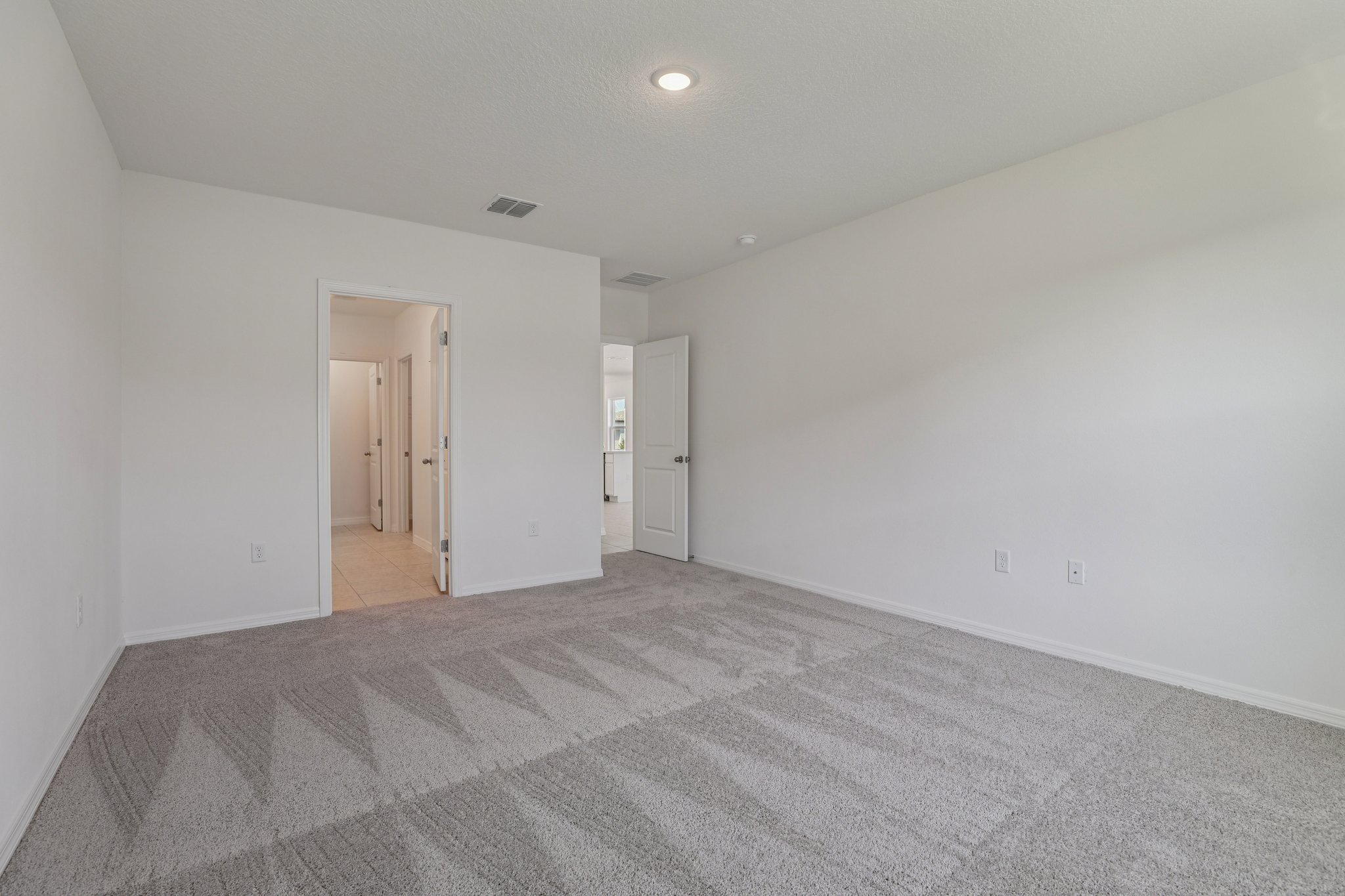 Empty white-walled room with clean light gray carpet and a doorway leading to a tiled hallway.