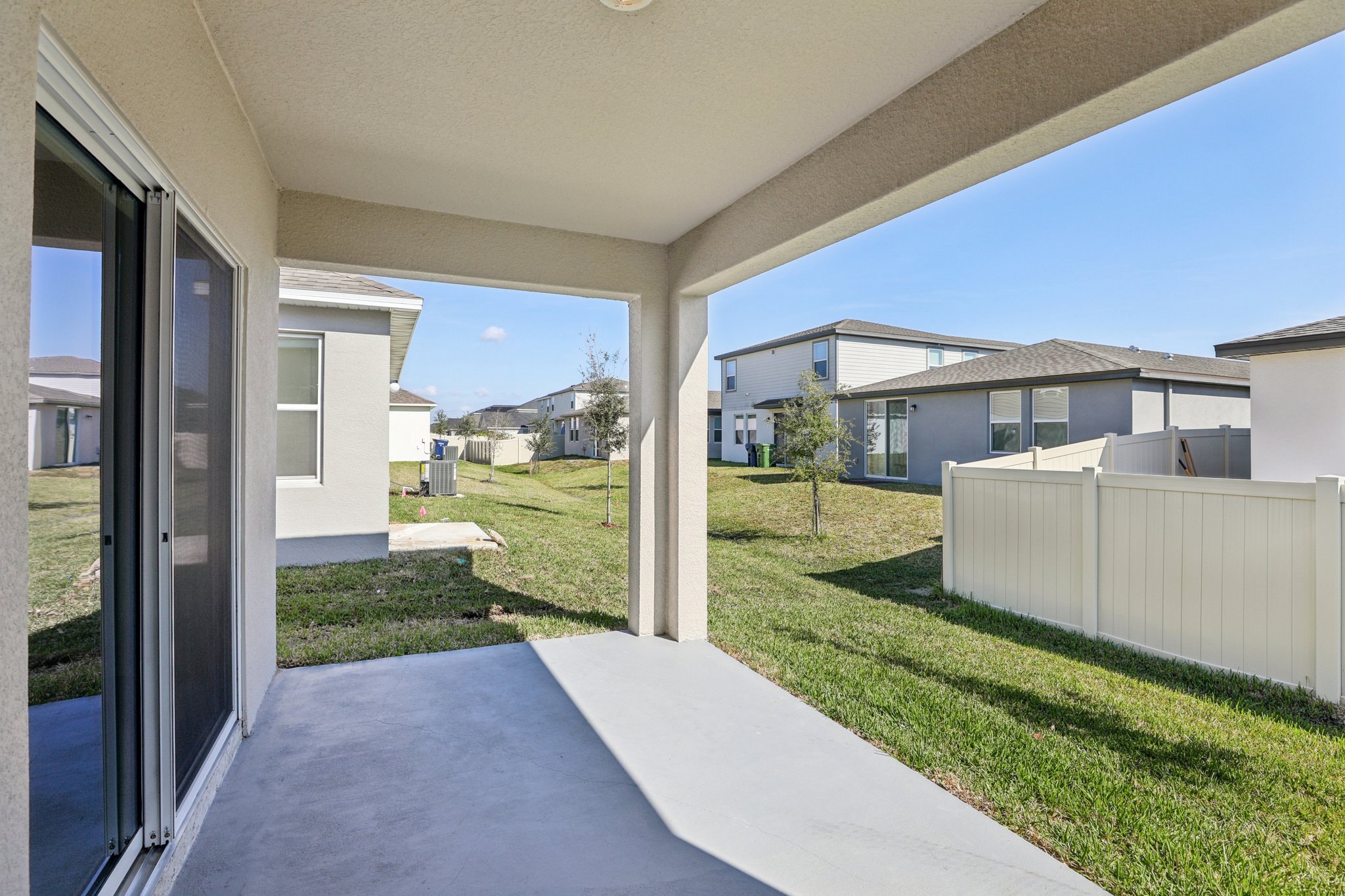 Covered outdoor patio overlooking a grassy backyard and neighboring modern houses, perfect for relaxation.