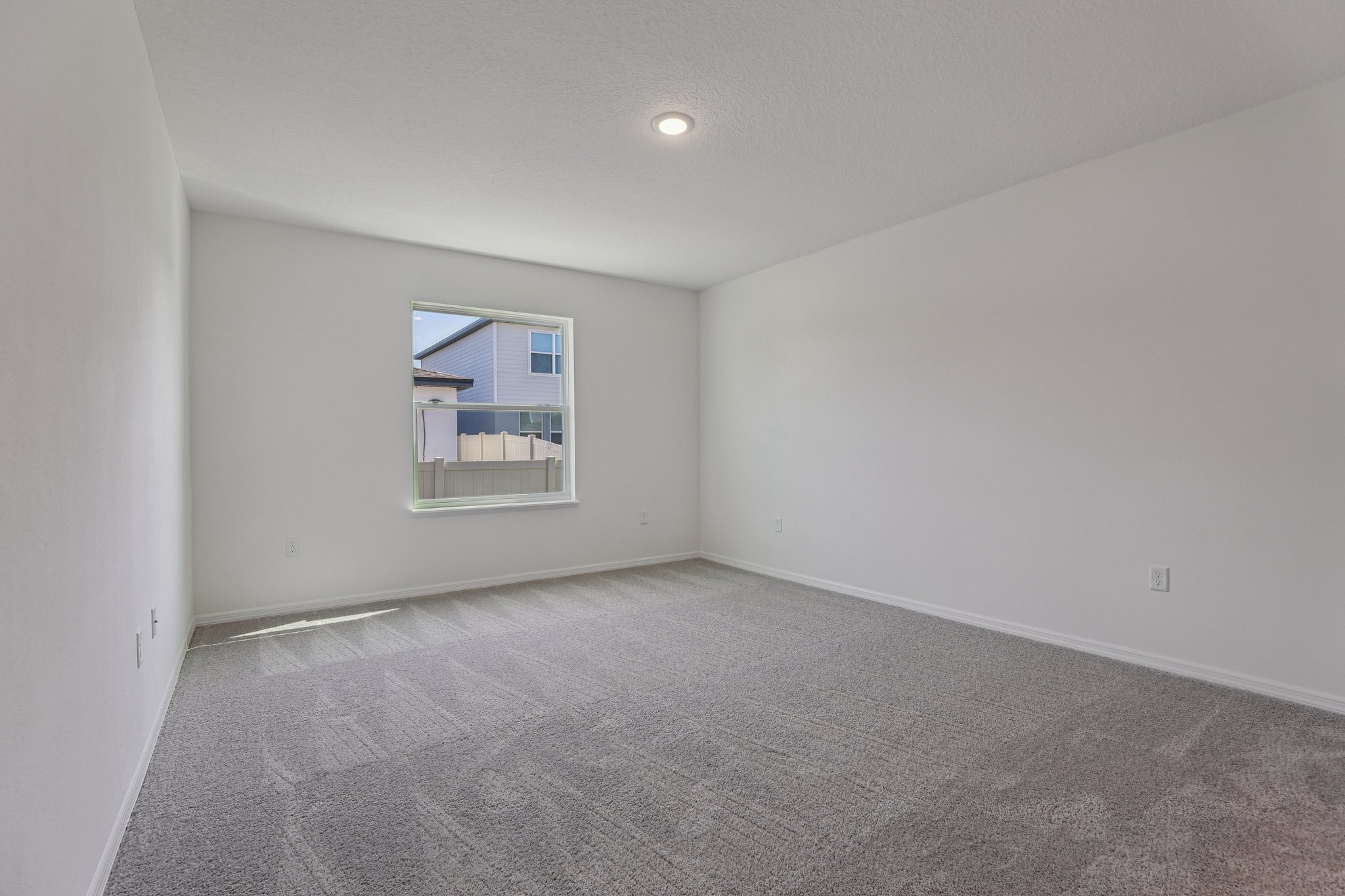 Empty white-walled room with carpet flooring and a large window offering natural light, perfect for real estate listings.