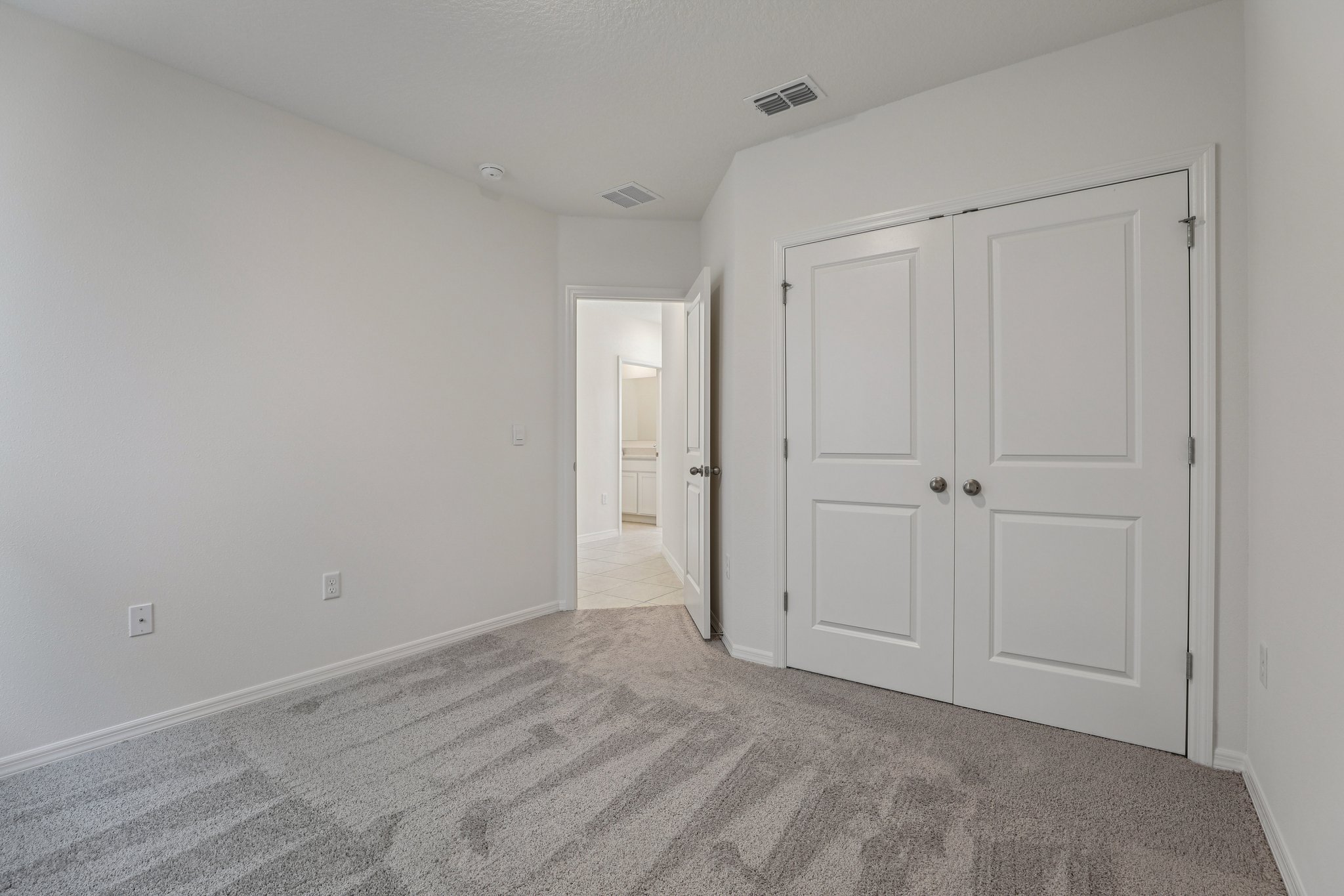 Empty room with gray carpet, white walls, a closed closet, and an open door leading to a tiled hallway.