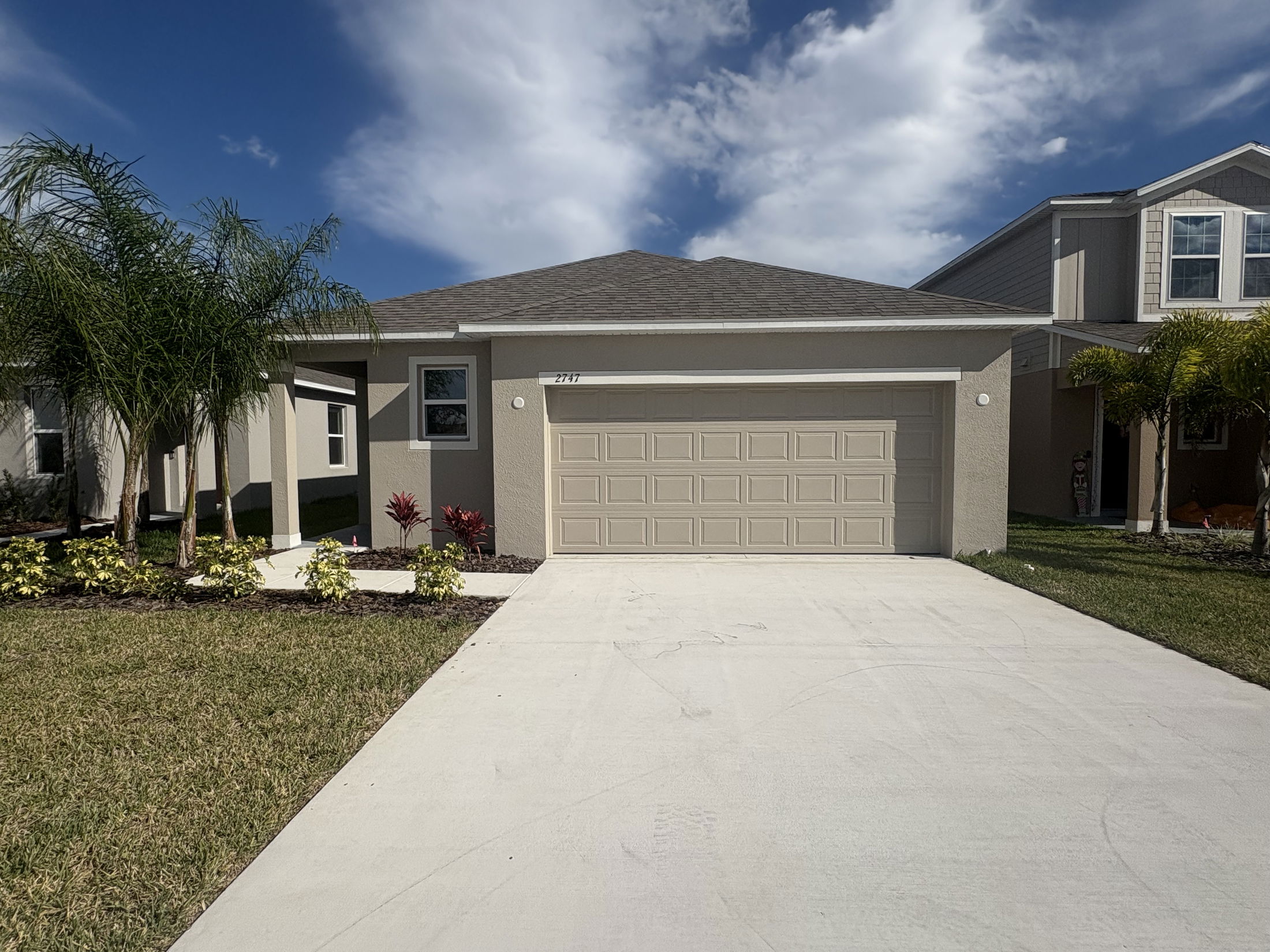 Modern suburban house with a garage and landscaped front yard under a blue sky.