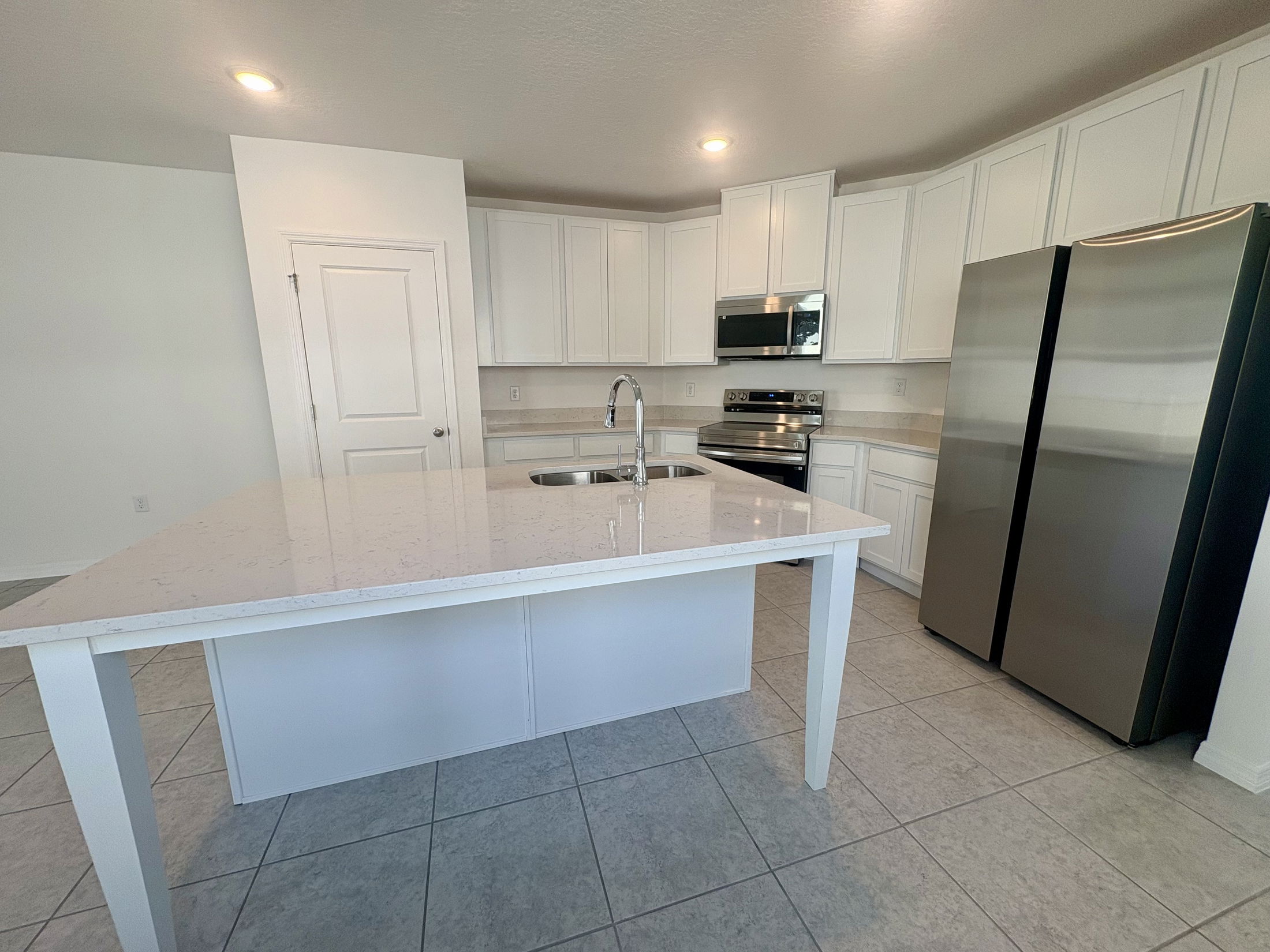Modern kitchen with white cabinets, stainless steel appliances, and a large central island with a marble countertop.