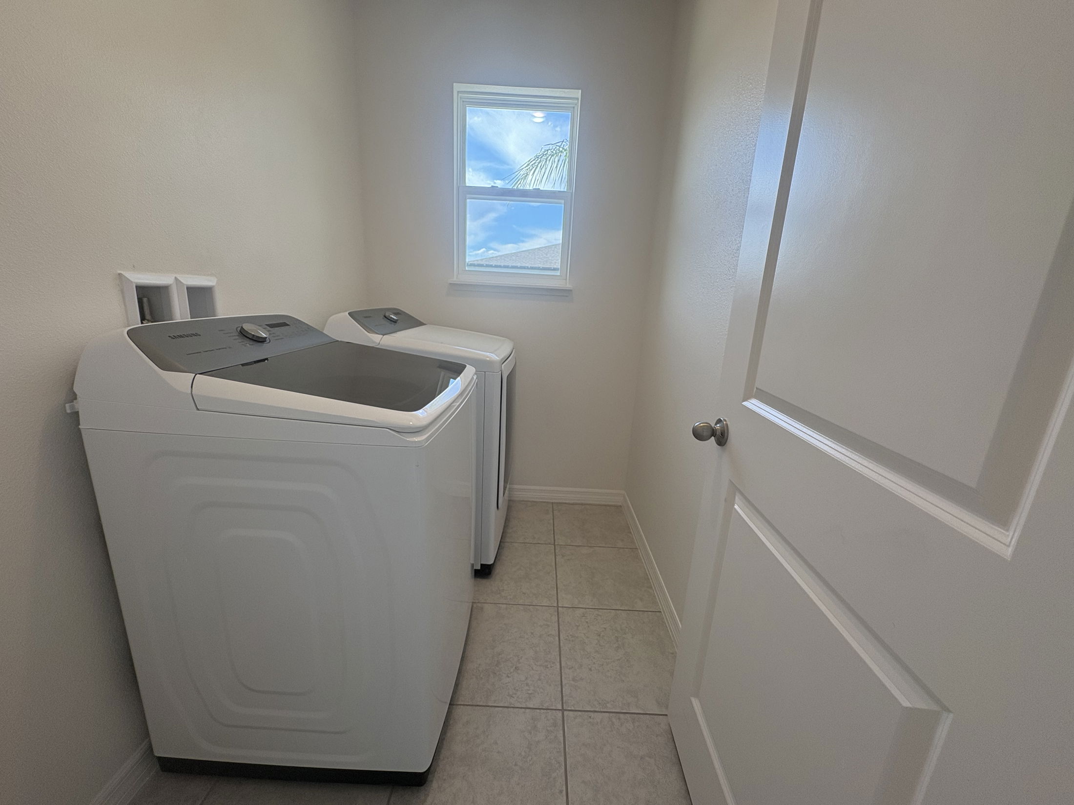 A modern laundry room featuring a Samsung washer and dryer set beneath a small window.