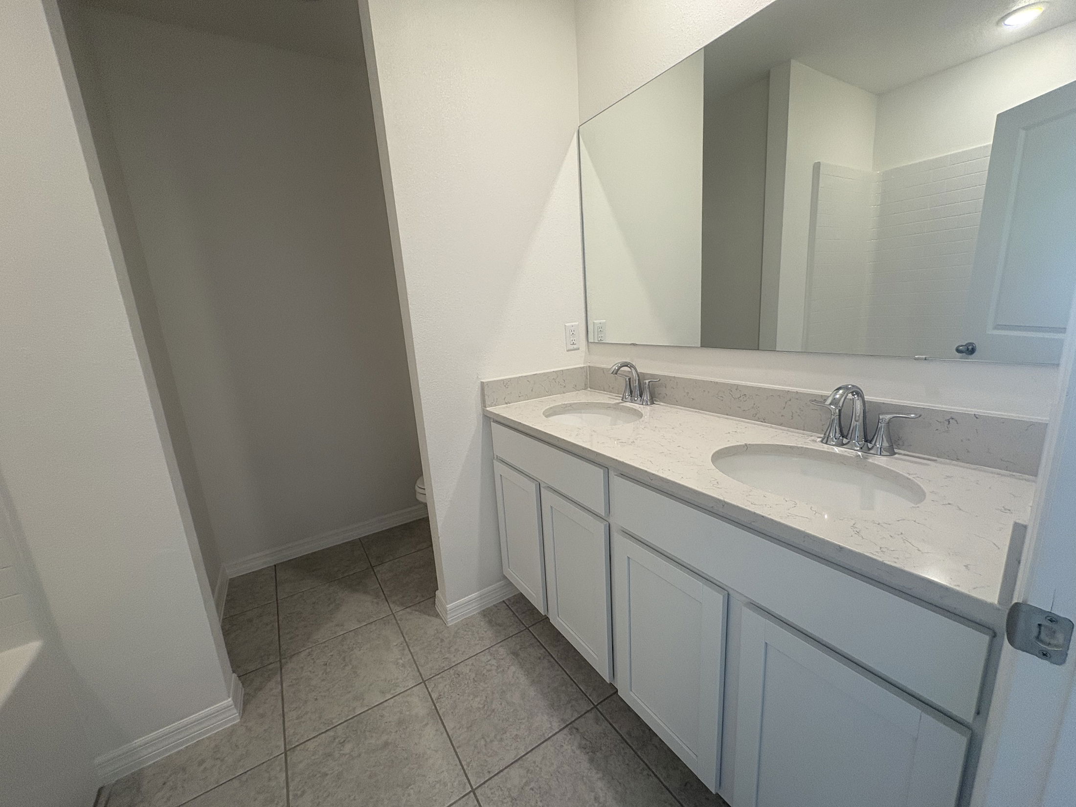 Modern bathroom with dual sinks, marble countertop, and large wall mirror on tiled floor.