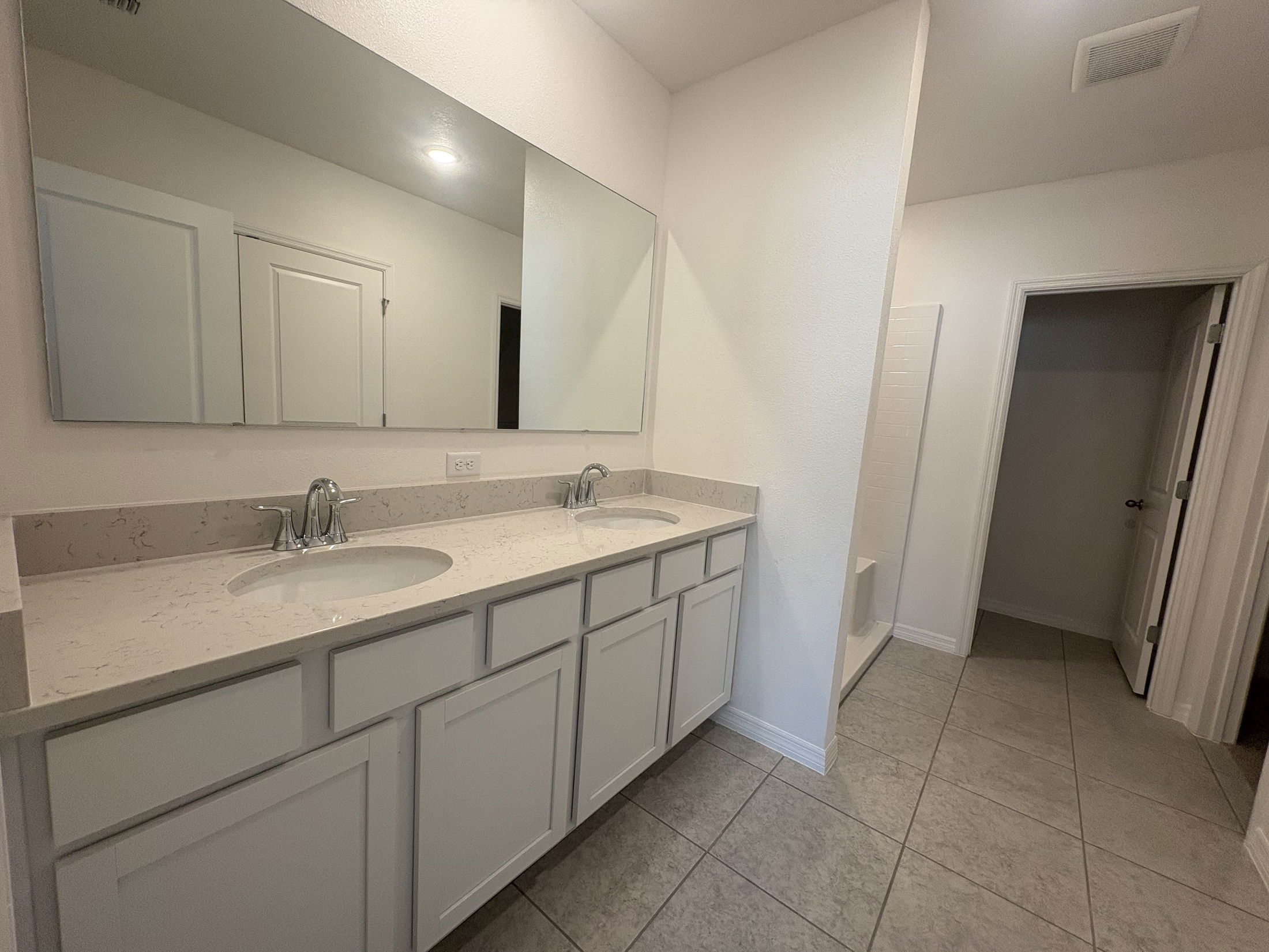 Modern bathroom with a double-sink vanity, large mirror, and tiled flooring.