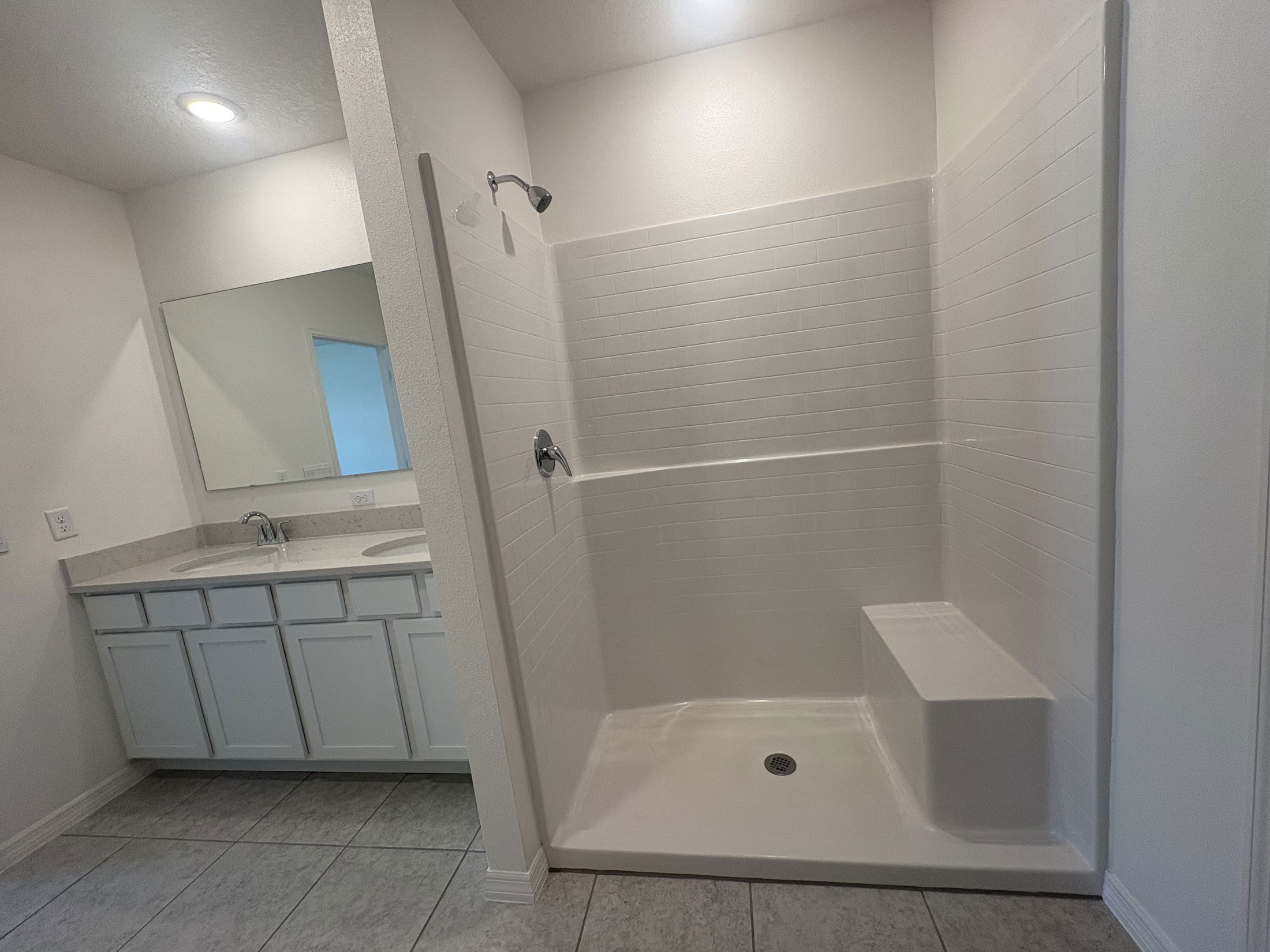 Modern bathroom with a spacious walk-in shower, bench seating, double sink vanity, large mirror, and tile flooring.