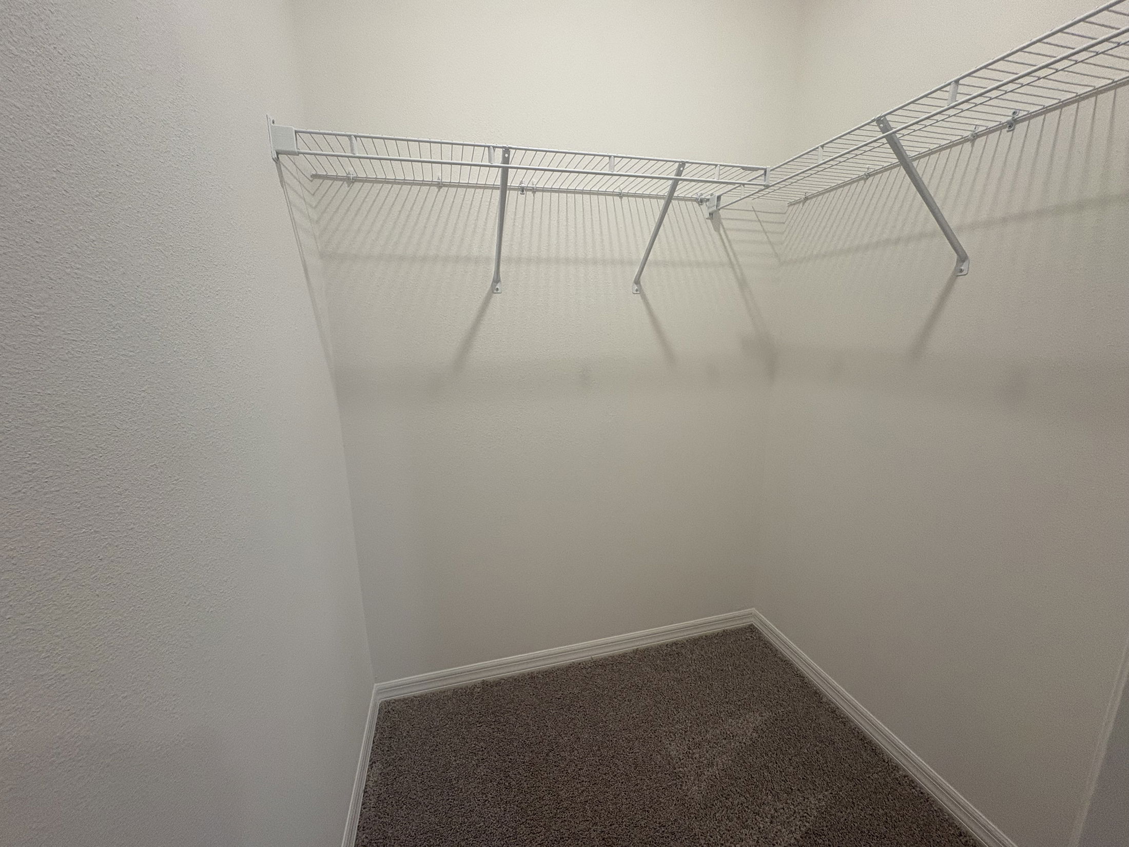 Empty walk-in closet with carpet flooring and wire shelving on white walls.