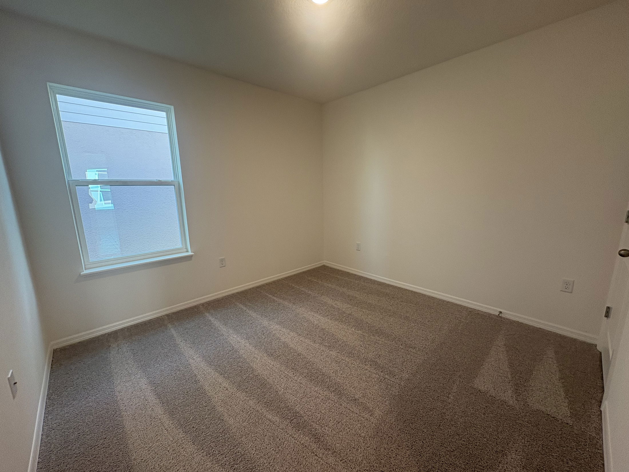 Empty room with beige carpet and a large window, featuring white walls and ceiling.