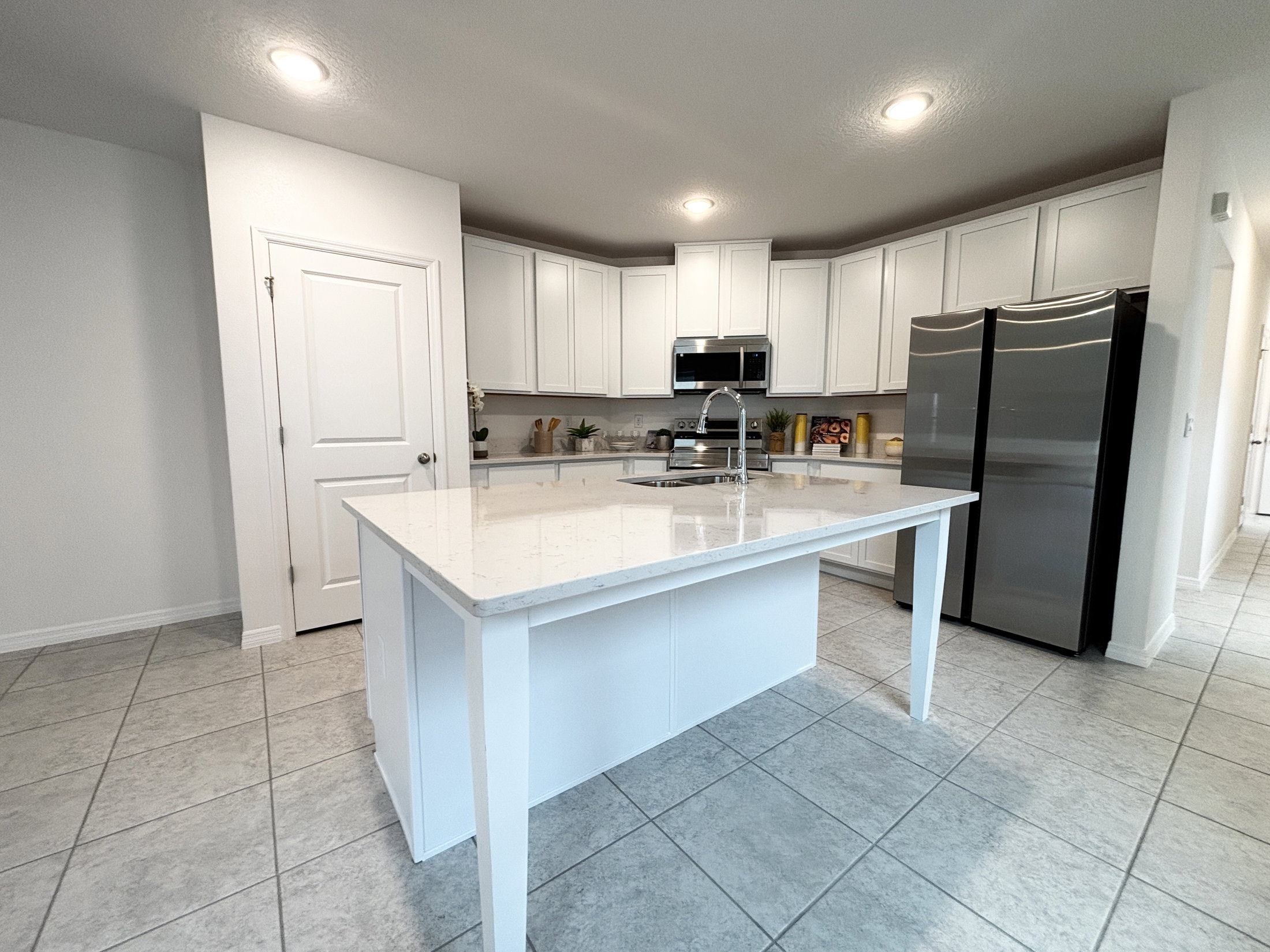 Modern kitchen design featuring white cabinetry, a spacious island, stainless steel appliances, and tiled flooring.