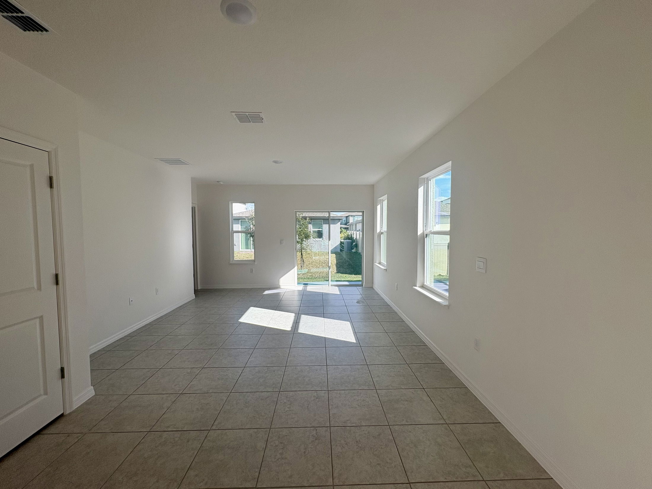 Bright and spacious living room with tile flooring and large windows overlooking the backyard.