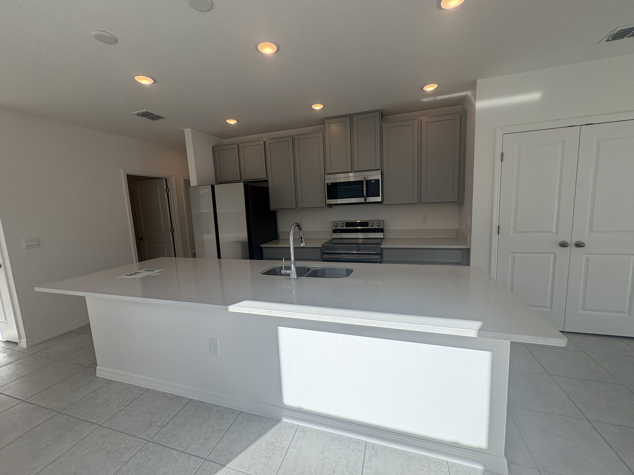 Modern kitchen with a large quartz island, stainless steel appliances, and gray cabinets under recessed lighting.