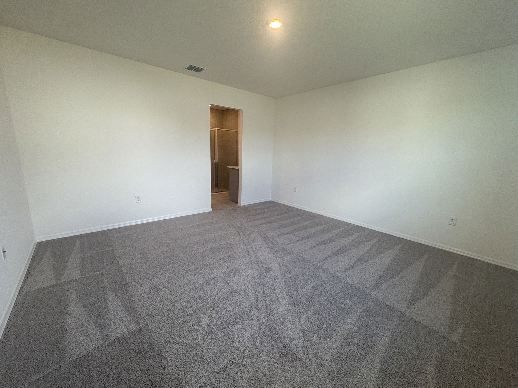 Spacious and empty living room with light gray carpet and soft natural lighting.