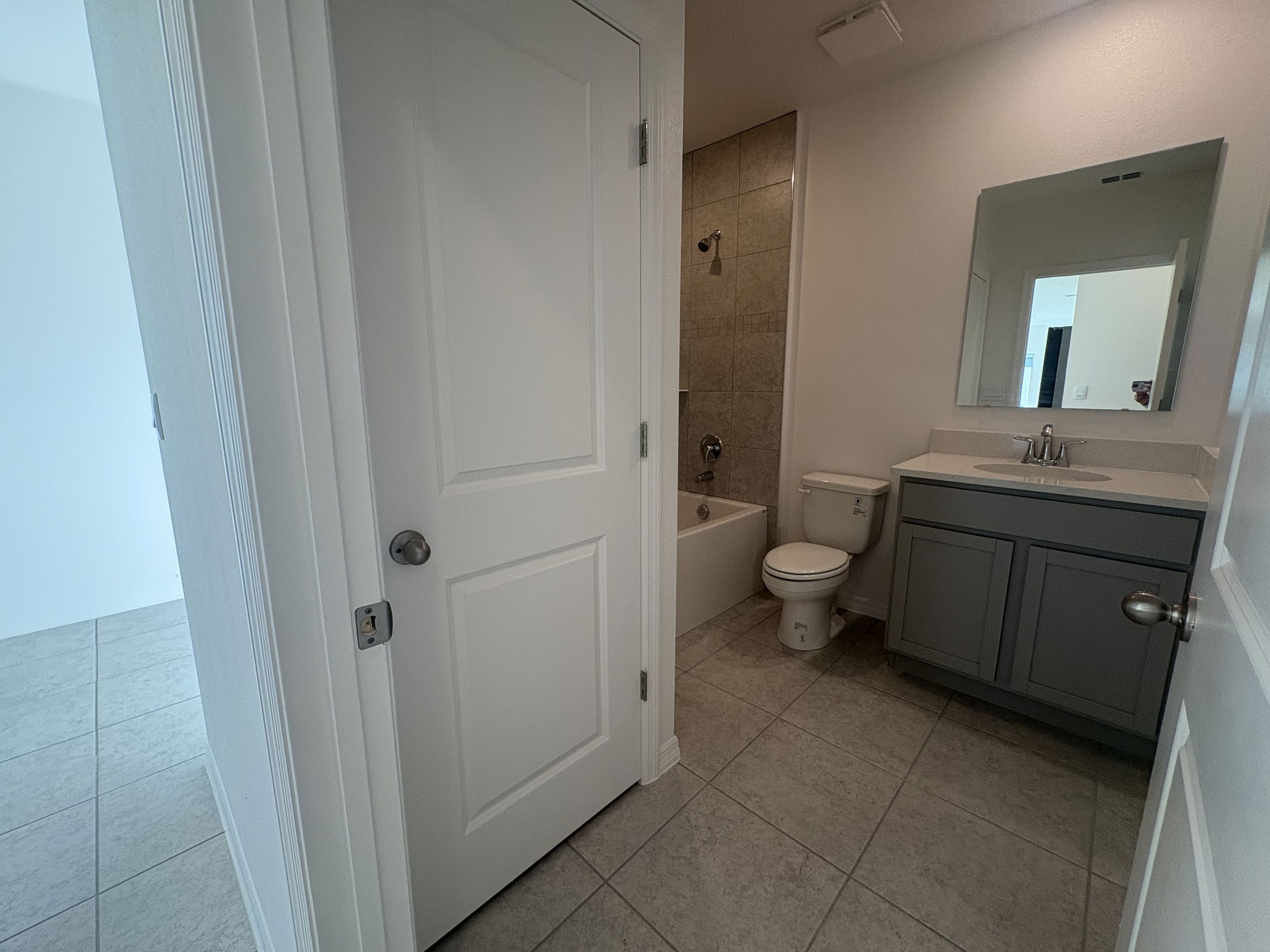 Modern bathroom with tiled floor, featuring a bathtub, toilet, and vanity with mirror.