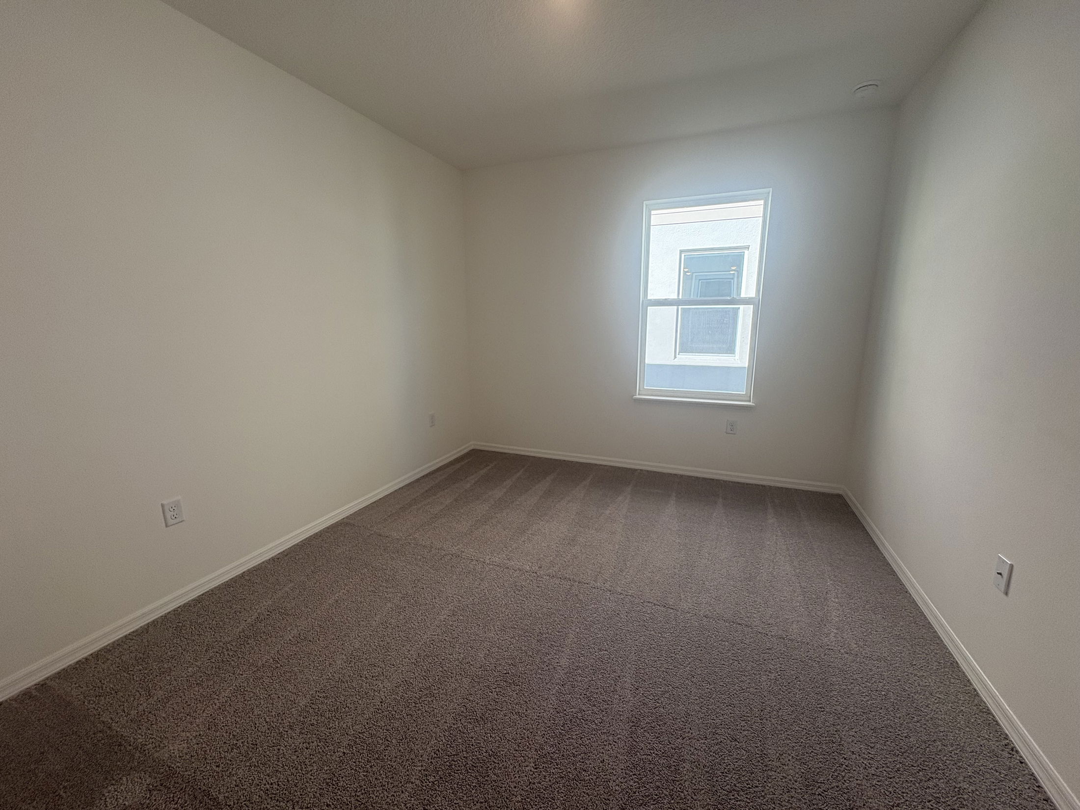 Empty carpeted room with a single window and light-colored walls.
